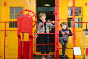 Two kids on the back platform of a yellow Caboose
