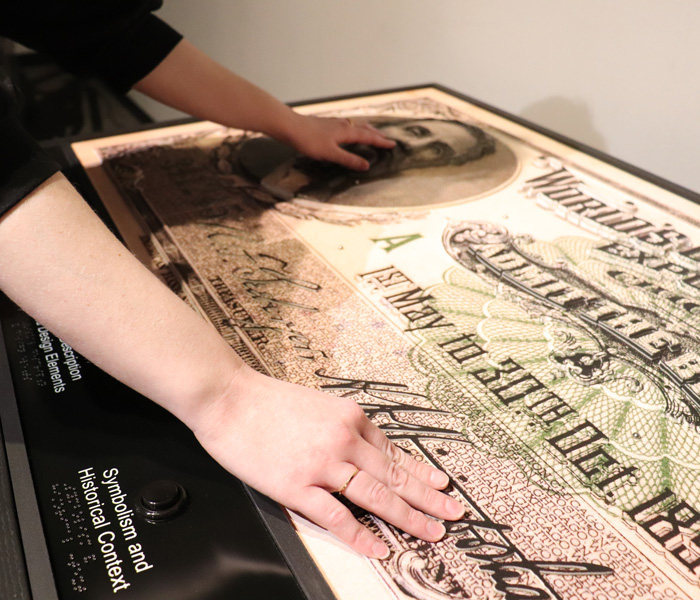 A museum guest swipes her hands on a money object featuring Lincoln