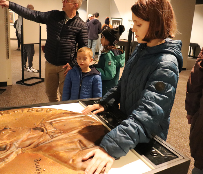 A museum guest touches a penny coin object featuring Lincoln