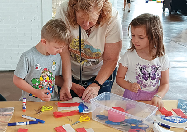 A woman and two children work together on a colorful craft project at a table.